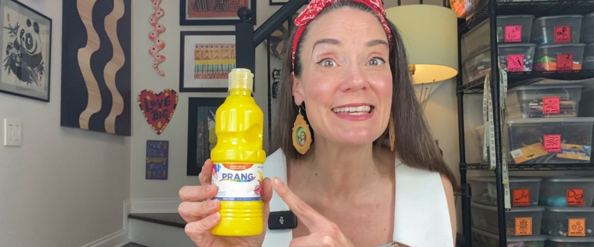 Cheerful artist showcasing Prang yellow paint in a colorful studio setting.