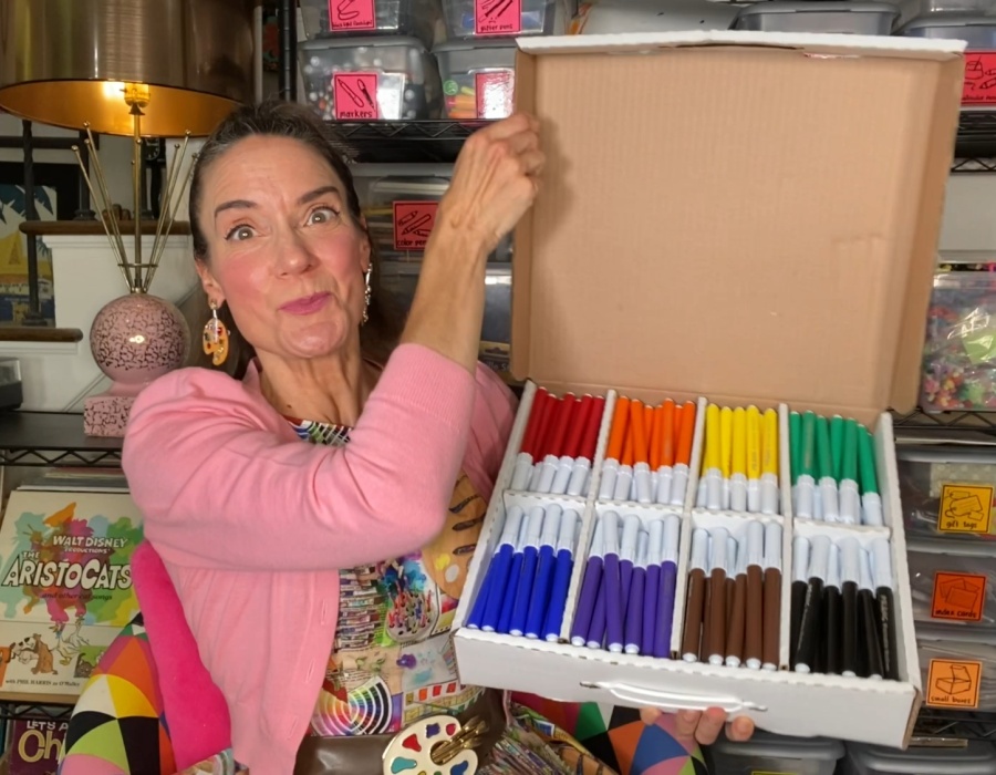 Woman holding markers in a box, colorful art supplies for creative projects.