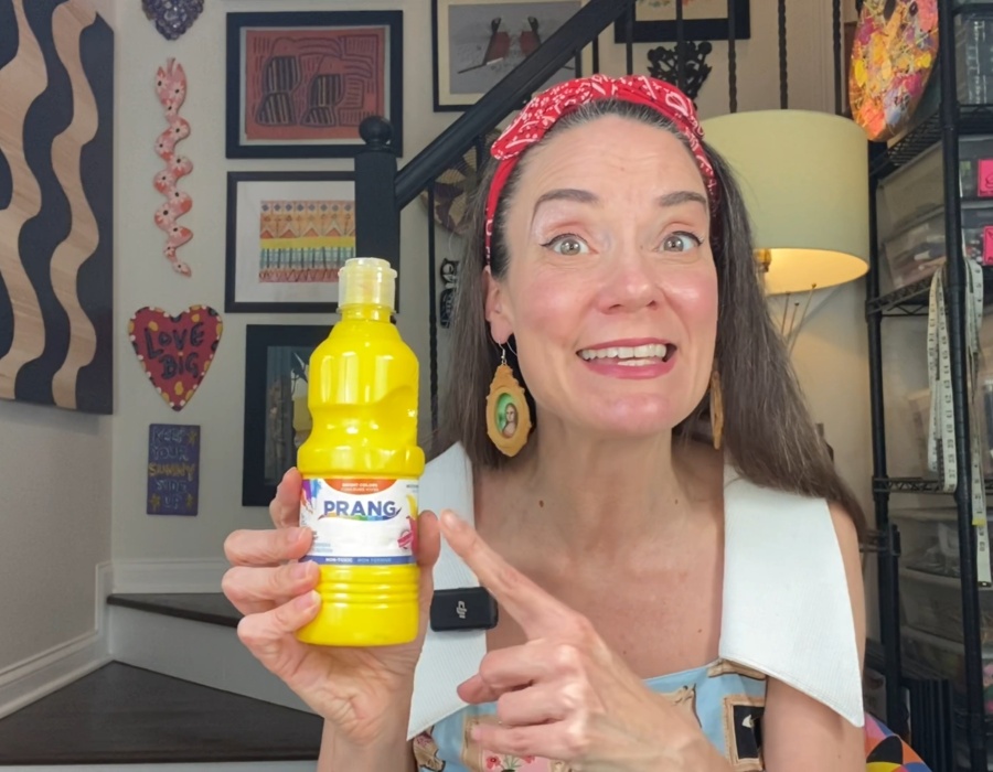 Cheerful artist showcasing Prang yellow paint in a colorful studio setting.