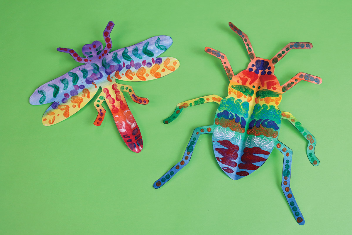Colorful paper insects on a vibrant green background, showcasing artistic creativity.