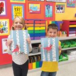 Two children proudly hold up their bird art projects crafted from Medium Weight Construction Paper in a colorful classroom filled with various activities and storage bins in the background.